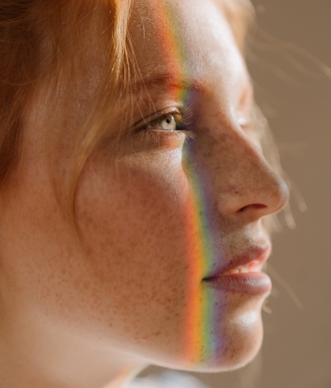 A close-up of a young woman with light green eyes, freckles, and red hair